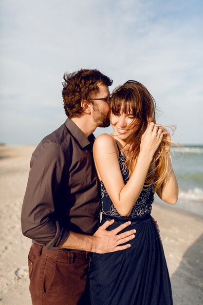 Romantisch paar omhelzen op het strand van de avond in de buurt van de oceaan. Elegante vrouw in blauwe jurk knuffelen haar vriendje met tederheid.