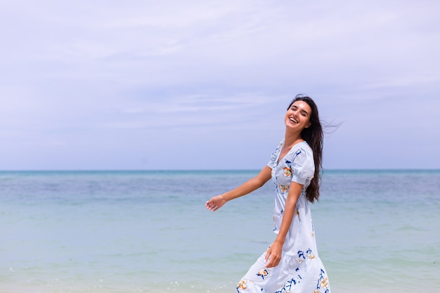 Romantisch portret van vrouw in lange blauwe jurk op strand door zee op winderige dag