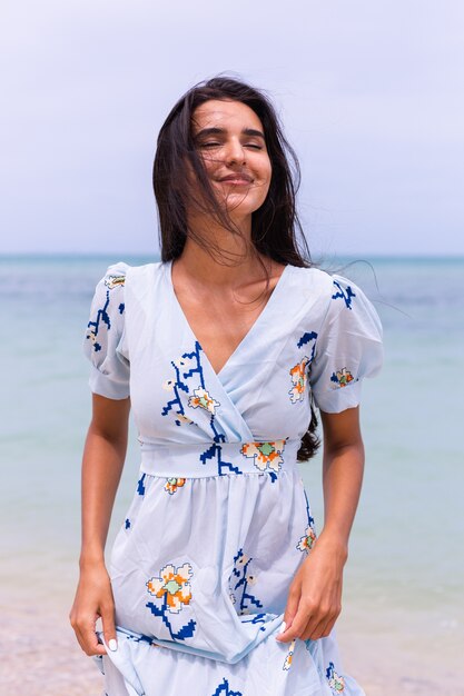 Romantisch portret van vrouw in lange blauwe jurk op strand door zee op winderige dag