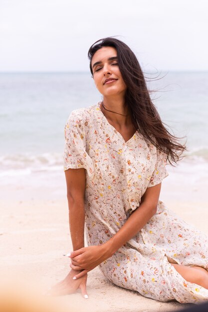 Romantisch portret van vrouw in lange jurk op strand op winderige bewolkte dag.