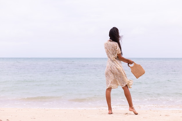 Romantisch portret van vrouw in lange jurk op strand op winderige bewolkte dag.