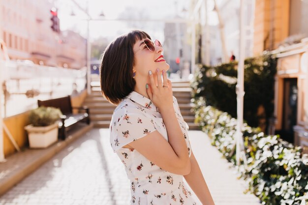 Romantische bruinharige vrouw die lacht op straat in het weekend. Buiten schot van verfijnd vrouwelijk model met kort kapsel dat positieve emoties uitdrukt.