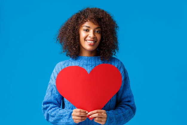 Romantische en sensuele schattige afro-amerikaanse vrouw met afro kapsel, met groot rood hartteken en glimlachend.