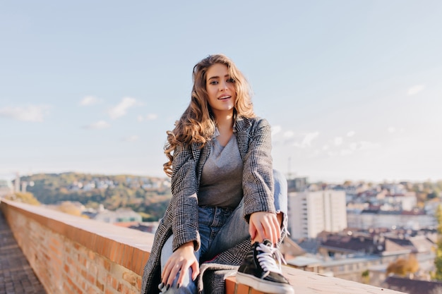 Romantische vrouw met lang krullend haar poseren met verbaasde gezichtsuitdrukking op hemelachtergrond