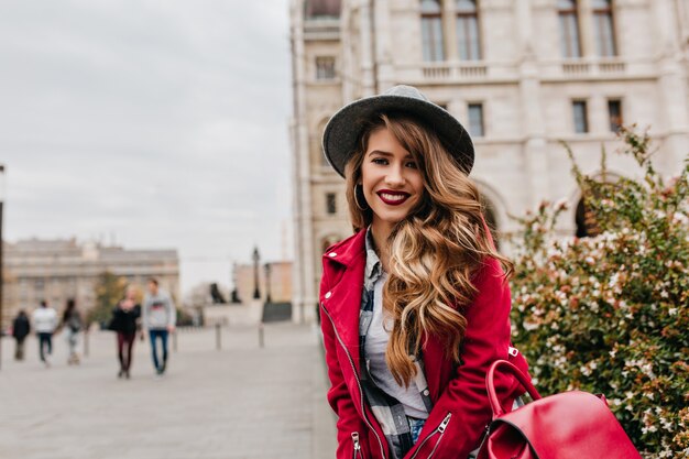 Romantische vrouw met lang krullend kapsel poseren met glimlach tijdens reizen door Europa