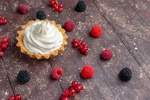 romige heerlijke cake samen met verschillende bessen verspreid over het bruine bureau, bessen-fruitcrème bakkoekje