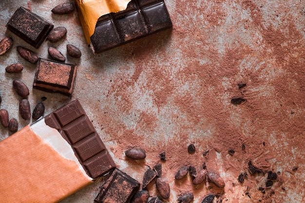 Rommelige tabel met cacaobonen en chocoladereep en stukken op rustieke tafel