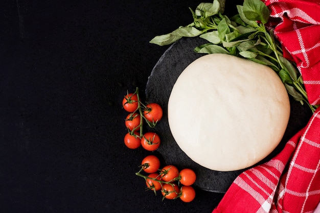 Rond vers brooddeeg; Cherry-tomaten; basilicum en servet op zwarte achtergrond