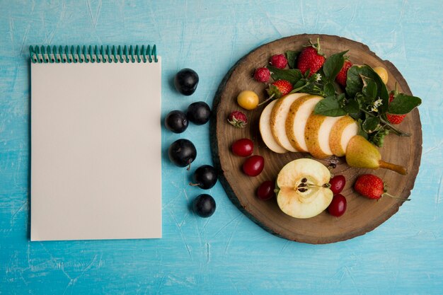 Ronde fruitschaal met peren, appel en bessen met een notitieboekje opzij