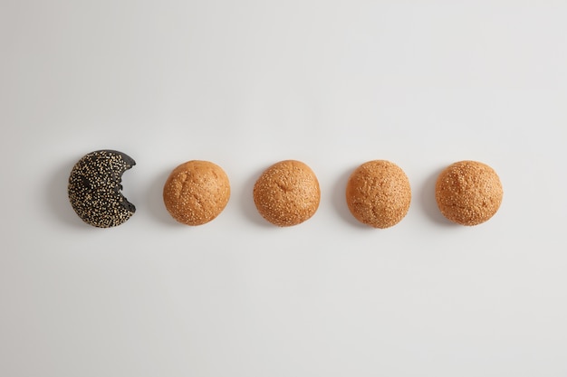 Ronde kleine biologische hamburgerbroodjes zonder gist met sesam op een witte ondergrond. Glutenvrij gezond product. Een zwarte is gebeten. Snel voedselconcept. Bakkerij en voeding. Smakelijke brioches.