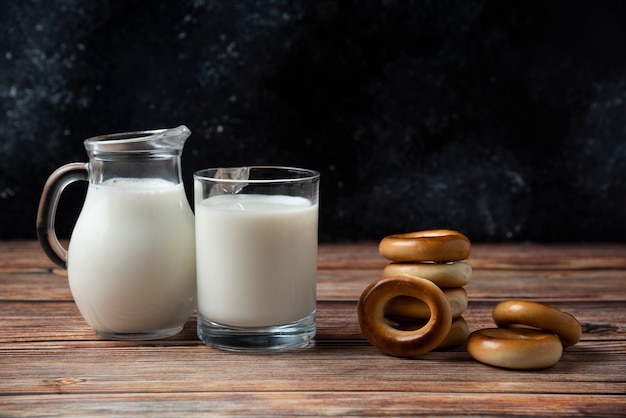 Ronde koekjes, glazen mok en kruik melk op houten tafel.