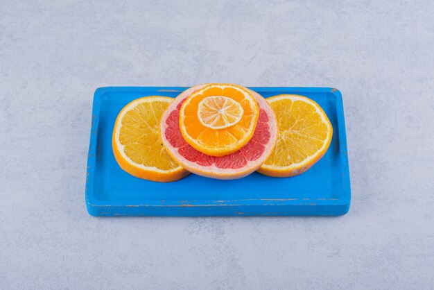 Ronde plakjes verse grapefruit, sinaasappel en citroen op blauw bord.