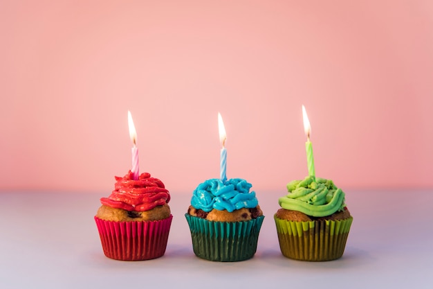 Rood; blauwe en groene cupcakes met een brandende kaarsen tegen roze achtergrond