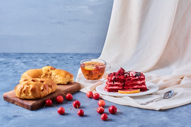 Rood fluweelcake met broodje en thee op een houten raad op blauw