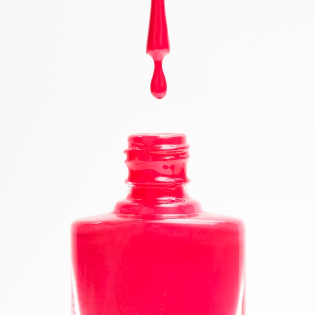 Rood nagellak dat in zijn fles tegen een witte achtergrond laat vallen