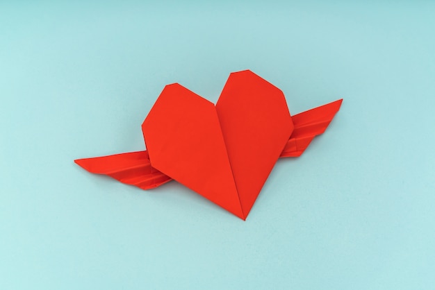 Rood papier origami hart met vleugels op blauwe achtergrond.