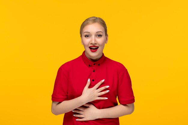 Rood shirt dag schattig gelukkig meisje houdt haar borst vast en lacht in een rood shirt op een gele achtergrond