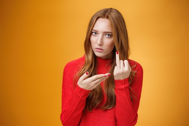 Gratis foto roodharig meisje vraagt waar de trouwring het zat is om te wachten op voorstel om vinger uit te strekken en ernaar te wijzen, ondervraagd en boos ruzie met vriendje over oranje achtergrond