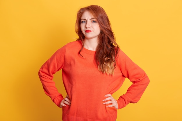 Roodharig wijfje dat oranje sweater met verbaasde gelaatsuitdrukking draagt