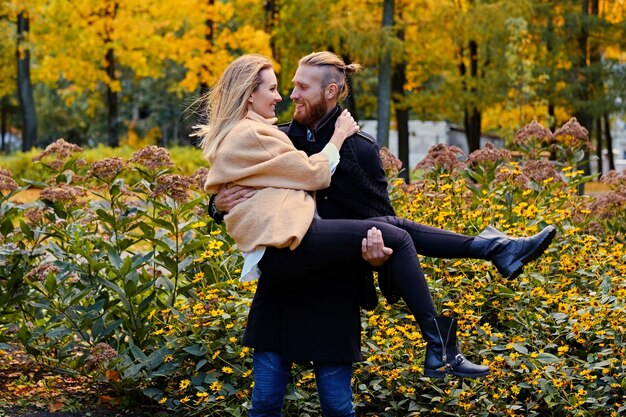 Roodharige bebaarde man houdt in zijn armen schattige blonde vrouw in een herfstpark.