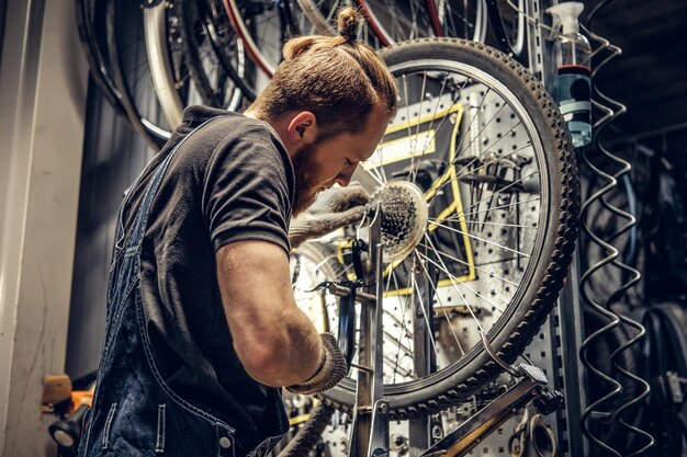 Roodharige, bebaarde monteur die de achterste cassette van de fiets verwijdert in een werkplaats.