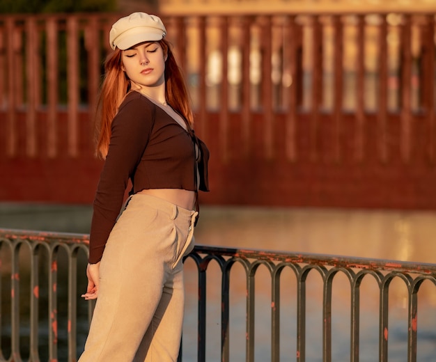 Roodharige jonge vrouw in een hoed die zich voordeed tijdens de zonsondergang in het park