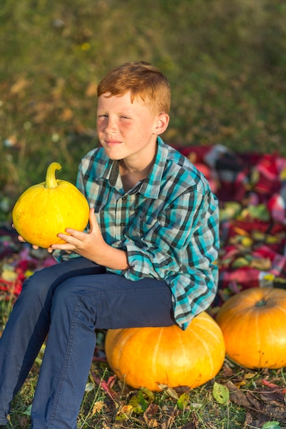 Gratis foto roodharige jongen zittend op een gele pompoen