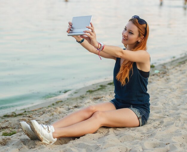 Roodharige sexy vrouw met tabletcomputer op een strand.