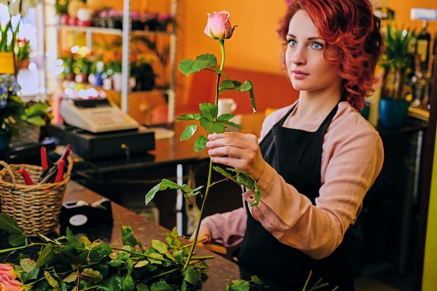 Roodharige vrouw houdt roze roos in een marktwinkel.