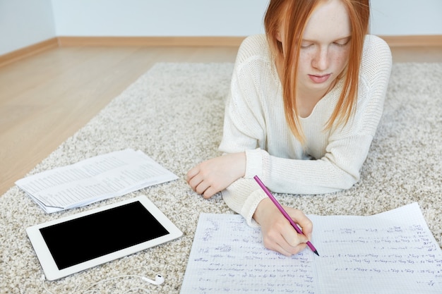 Roodharige vrouw liggend op de vloer met notitieboekje en tablet