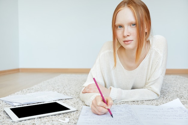 Roodharige vrouw liggend op de vloer met notitieboekje en tablet