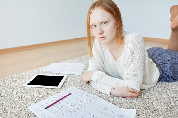 Roodharige vrouw liggend op de vloer met notitieboekje en tablet