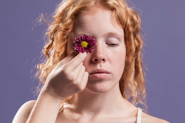 Roodharigevrouw die een bloem over haar oog houden