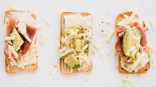 Rooster sneetjes brood met geraspte kaas; ham en avocado slice op witte achtergrond