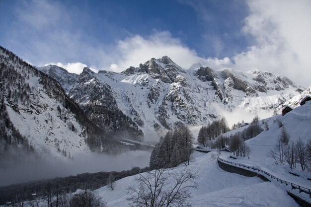 Rotsachtige berg bedekt met sneeuw en mist tijdens de winter met een blauwe lucht