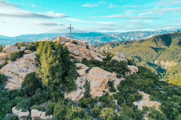 Rotsachtige klif bedekt met groen met een kruis op de top en prachtige bergen