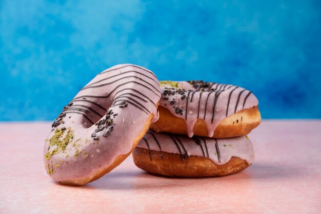 Roze aardbei donuts versierd met chocoladestukjes op roze tafel.