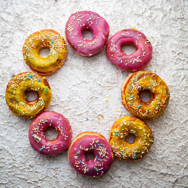 Roze en gele donuts in de vorm van een cirkel op een witte gestructureerde achtergrond. bovenaanzicht.