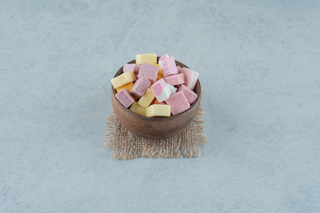 Roze en gele marshmallow-snoepjes in een houten kom op een witte ondergrond