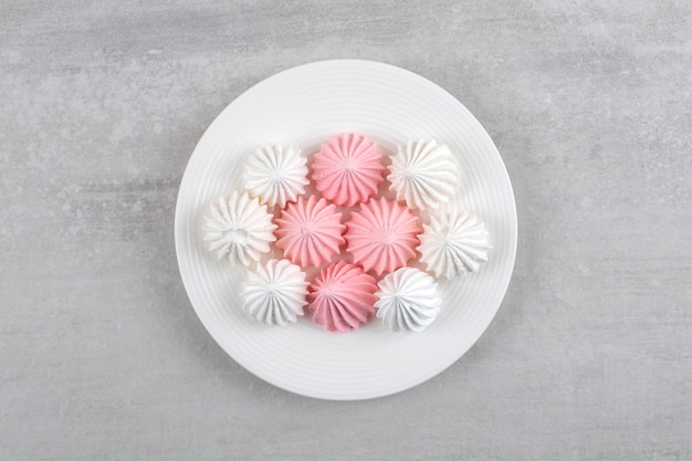 Roze en witte meringue op een witte plaat, op de marmeren tafel.