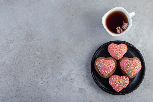 Roze koekjes in gehoorde vorm met thee op grijze achtergrond.