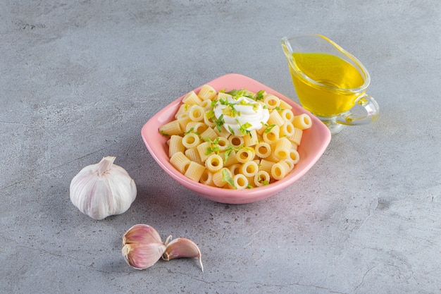 Roze kom heerlijke gekookte pasta met olijfolie op stenen oppervlak.