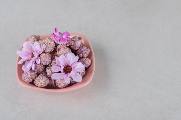 Roze kom vol gearomatiseerde popcorn versierd met bloemen op marmeren tafel.