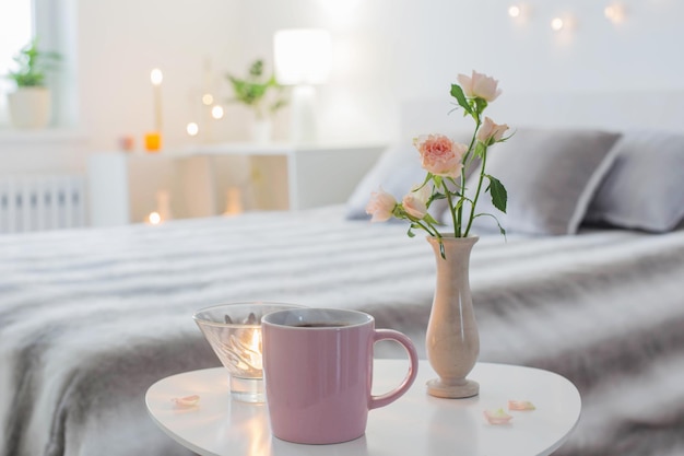 Roze kopje koffie en rozen in vaas op tafel in slaapkamer