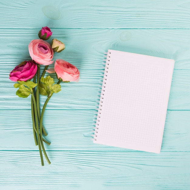 Roze nam bloemen met leeg notitieboekje op houten lijst toe