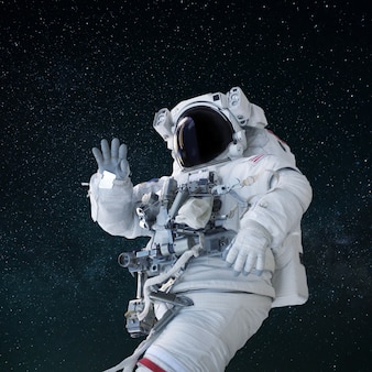Ruimteman in een pak met een helm zwaait met zijn hand en groet in de open ruimte. hallo concept. astronauten reizen Premium Foto