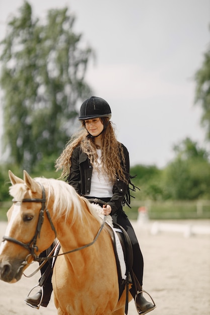 Gratis foto ruitervrouw die haar paard berijdt op een boerderij. vrouw heeft lang haar en zwarte kleding. vrouwelijke ruiter op haar bruin paard.