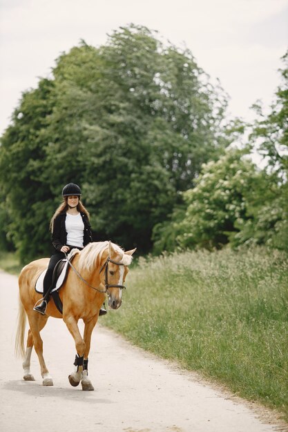 Ruitervrouw die haar paard berijdt op een boerderij. Vrouw heeft lang haar en zwarte kleding. Vrouwelijke ruiter op haar bruin paard.
