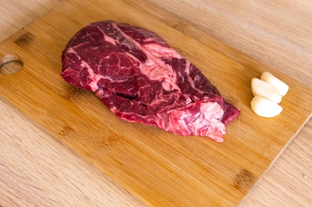 Rundvlees op houten snijplank bij keuken bovenaanzicht van ongekookte rauwe biefstuk met knoflook close-up del Premium Foto