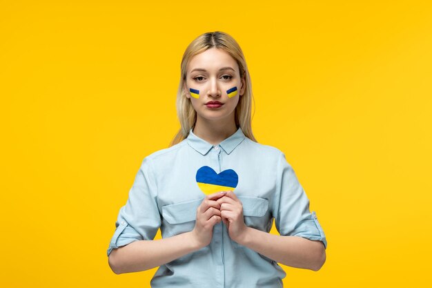 Russische Oekraïense conflict schattig meisje gele achtergrond met Oekraïense vlag op wangen met hart